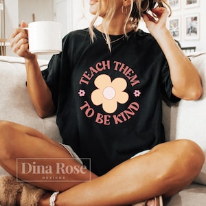 May include: A black t-shirt with a pink and yellow flower graphic and the text "Teach Them To Be Kind".