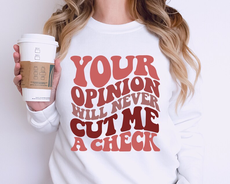May include: White sweatshirt with the text "YOUR OPINION WILL NEVER CUT ME A CHECK" in a retro font with pink, red, and brown colors.