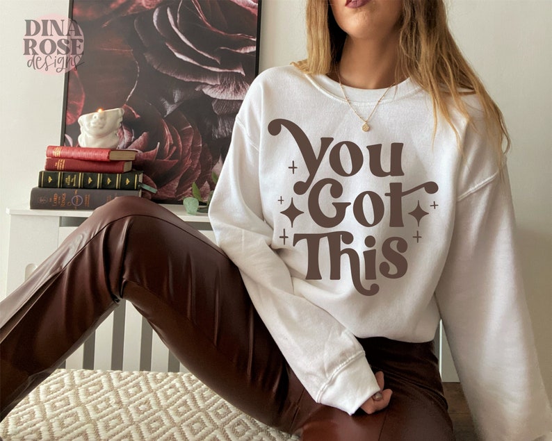 Puede incluir: Sudadera blanca con texto marr&oacute;n que dice "You Got This" en un estilo de fuente retro.