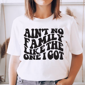 Pu&ograve; includere: Maglietta bianca con testo nero che recita "Ain't no family like the one I got" in un font retr&ograve;.