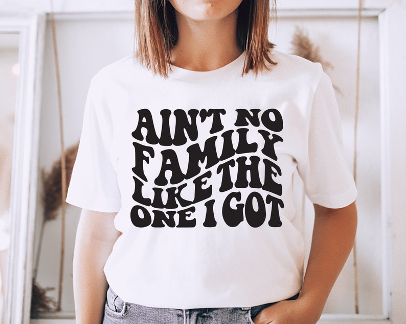 Pu&ograve; includere: Maglietta bianca con testo nero che recita "Ain't no family like the one I got" in un font retr&ograve;.