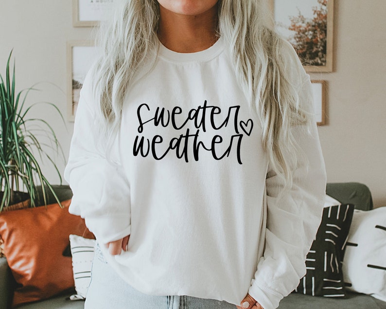 Puede incluir: Sudadera blanca con el texto "sweater weather" en letra negra con un peque&ntilde;o coraz&oacute;n.