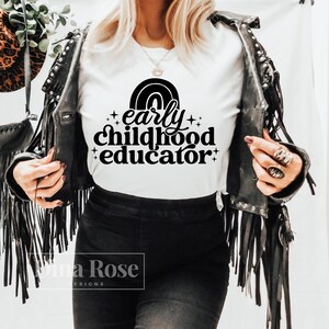 May include: White t-shirt with black text that reads "early childhood educator" with a rainbow graphic above the text.