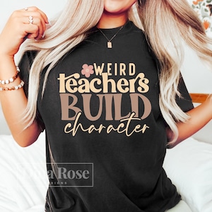 May include: Black t-shirt with the text "Weird teachers build character" in pink and brown lettering with a small pink flower graphic.