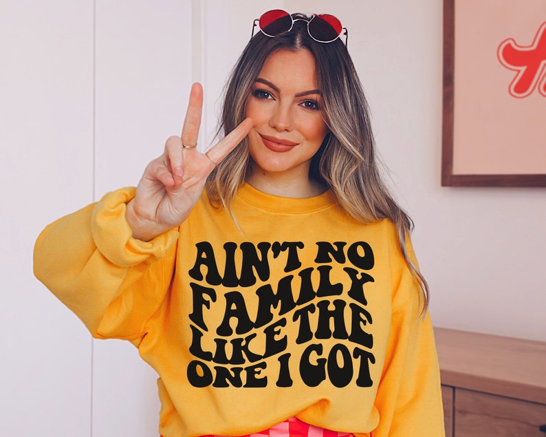 Pu&ograve; includere: Una felpa gialla con testo nero che recita "Ain't no family like the one I got" in un font retr&ograve;.