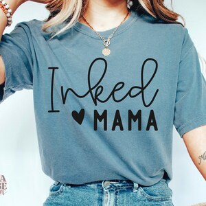 May include: A blue t-shirt with the text "Inked Mama" in black lettering with a small heart in between the words.