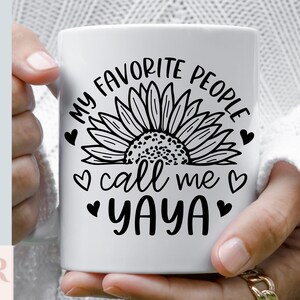 K&ouml;nnte beinhalten: Eine wei&szlig;e Keramiktasse mit einem schwarzen Sonnenblumenmuster und dem Text "Meine Lieblingsmenschen nennen mich Yaya".
