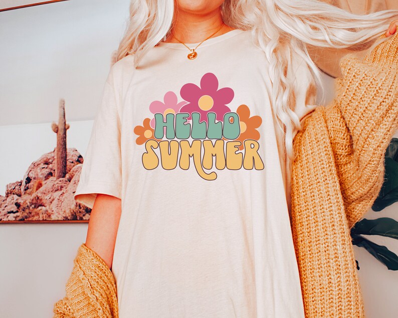 May include: A white t-shirt with a retro-style graphic that says "Hello Summer" in green, yellow, and orange letters. The graphic is surrounded by pink, orange, and yellow flowers.