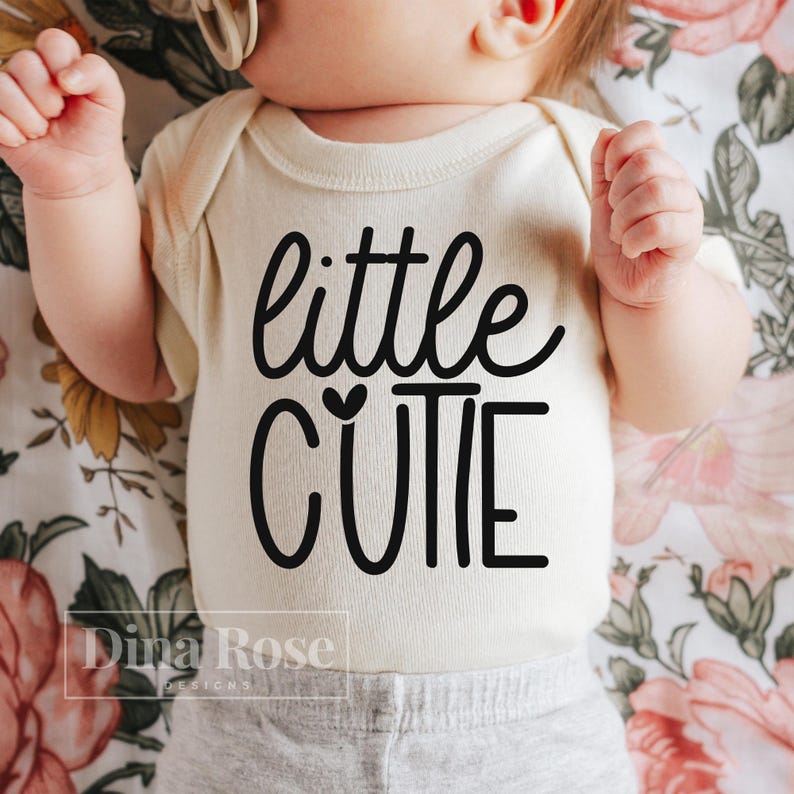 May include: A white onesie with black text that reads "little cutie" with a small heart above the word "cutie".