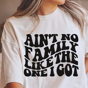 Pu&ograve; includere: Maglietta bianca con testo nero che recita "Ain't no family like the one I got" in un font retr&ograve;.