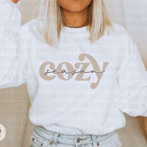 May include: White sweatshirt with a brown graphic that says "cozy season" in a retro font.