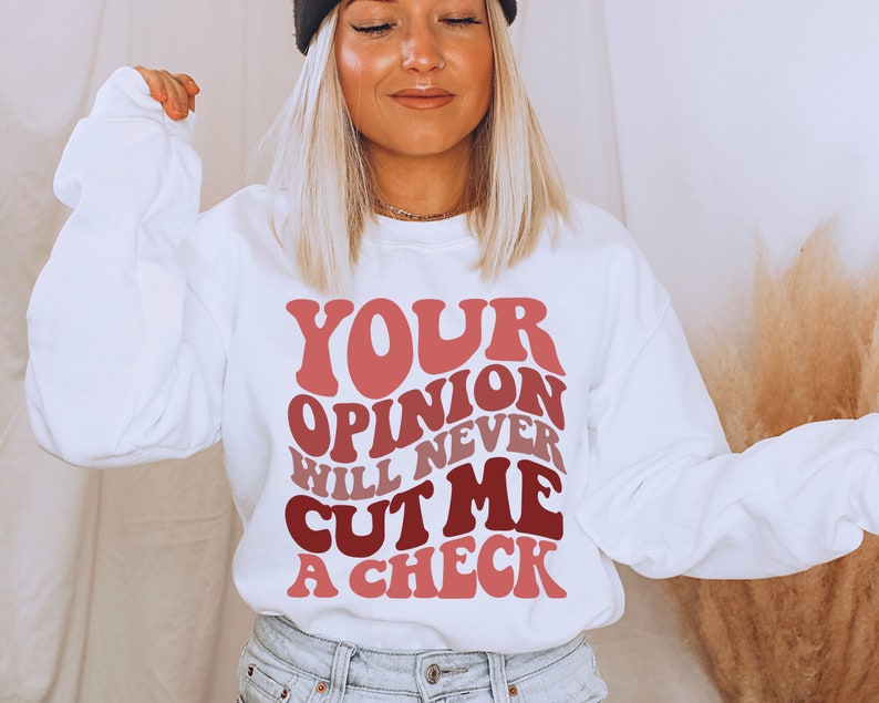 May include: White sweatshirt with a pink and red graphic that says "Your opinion will never cut me a check."