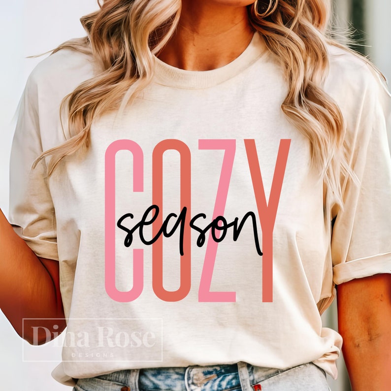 May include: A cream colored t-shirt with the text "COZY season" in pink and red lettering. The text is layered with the "COZY" letters in a larger font size than the word "season".