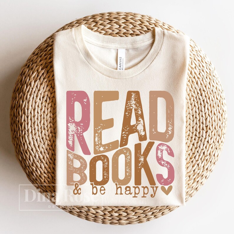 May include: A beige t-shirt with the text "READ BOOKS & be happy" in pink, brown, and orange with a distressed look. The text is centered on the shirt.