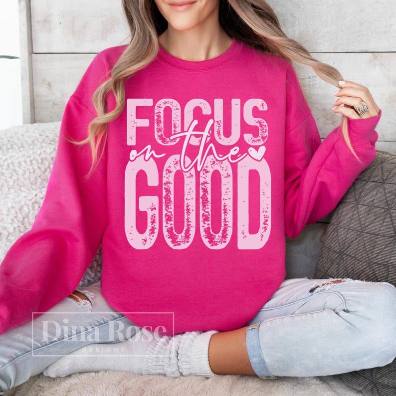 K&ouml;nnte beinhalten: Ein leuchtend pinkfarbenes Sweatshirt mit dem Schriftzug "FOCUS on the GOOD" in verblasster, hellerer rosa Schrift. Das Rundhals-Sweatshirt ist aus weichem Stoff. Das Design ist mittig auf der Vorderseite des Kleidungsst&uuml;cks platziert.