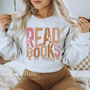 May include: A gray sweatshirt with the text "READ BOOKS & be happy" in pink, brown, and orange letters with a distressed look. The text is centered on the front of the sweatshirt.