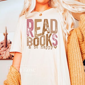 May include: A white t-shirt with the text "READ BOOKS & be happy" in pink, brown, and orange lettering. The text has a distressed look.