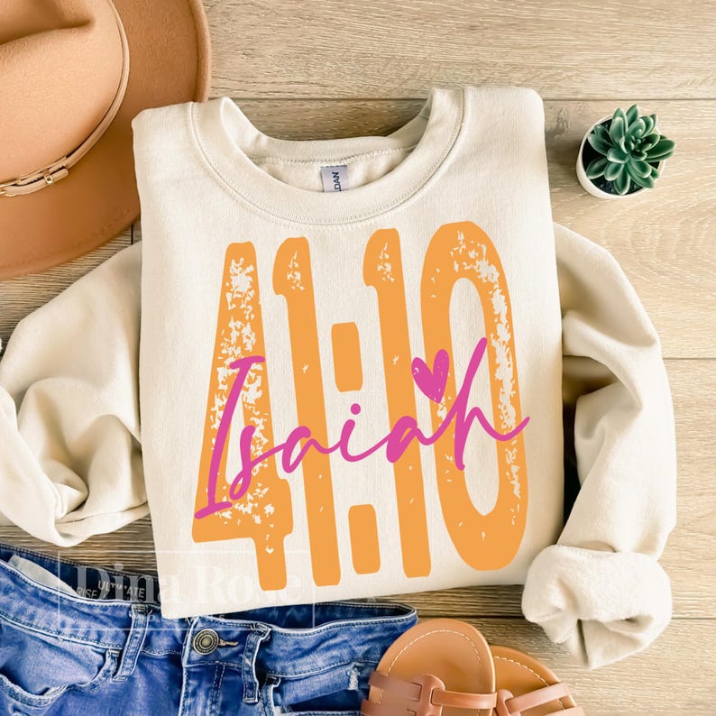 May include: Cream-colored sweatshirt with the text "41:10 Isaiah" in orange and pink. The design features a heart symbol. The sweatshirt is a casual style, suitable for everyday wear.
