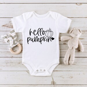 May include: White baby onesie with black text that reads "hello pumpkin" and a small black pumpkin graphic with a heart.
