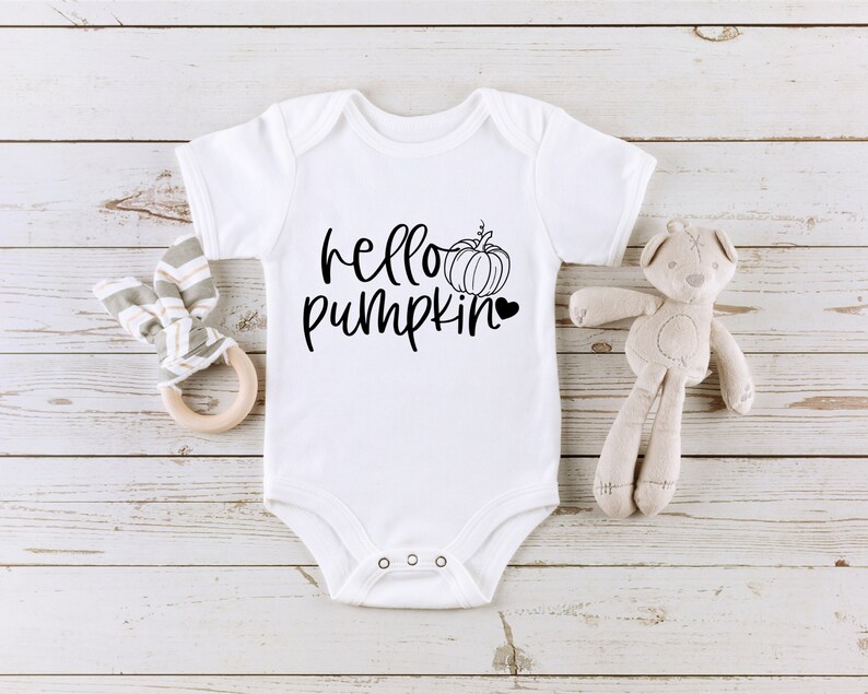 May include: White baby onesie with black text that reads "hello pumpkin" and a small black pumpkin graphic with a heart.