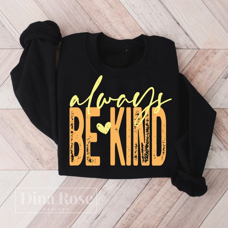 May include: Black sweatshirt with the words "always BE KIND" in yellow and orange lettering. The word "always" is in a cursive font, and the words "BE KIND" are in a block font. A small yellow heart is between the words "BE" and "KIND".