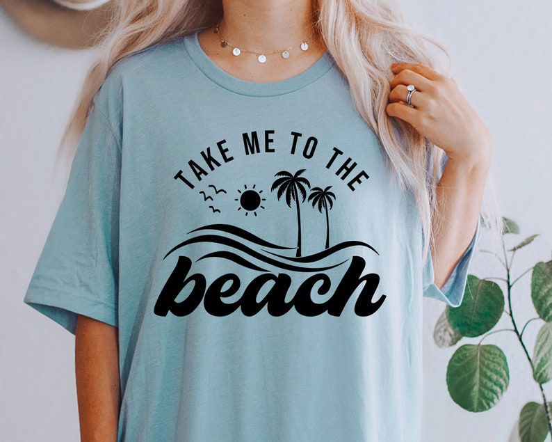 May include: A light blue t-shirt with the text "Take me to the beach" in black lettering. The design includes palm trees, a sun, and waves.