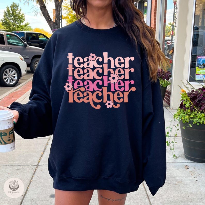 May include: Black sweatshirt with the text "teacher" repeated four times in a retro font with pink and orange accents and flowers.