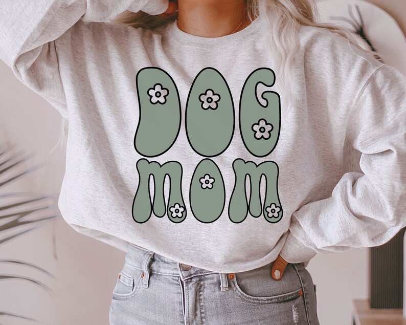 May include: A gray sweatshirt with the text "DOG MOM" in green and white. The letters are stylized with a retro 70s font and have small white flowers on them.