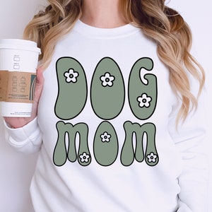 May include: White sweatshirt with a green and white graphic that says "Dog Mom" in a retro font.