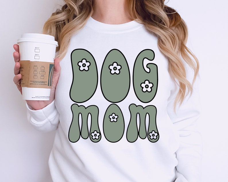 May include: White sweatshirt with a green and white graphic that says "Dog Mom" in a retro font.