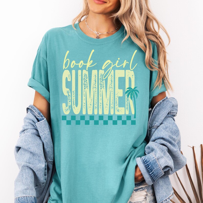 May include: Teal t-shirt with the words "book girl SUMMER" in a light yellow font. The word "SUMMER" has a palm tree graphic. A checkered pattern is at the bottom of the text.