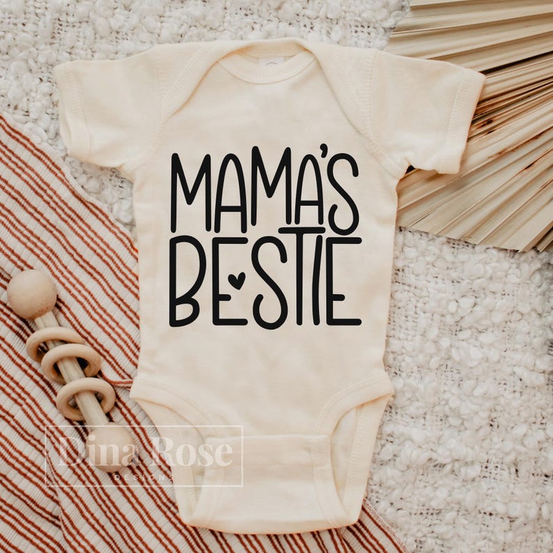 May include: A white baby onesie with black text that reads "Mama's Bestie".