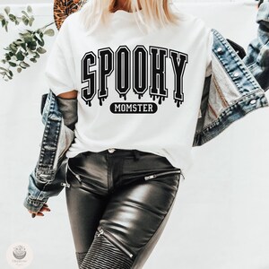 May include: White t-shirt with black text that reads "Spooky Momster" in a dripping font.