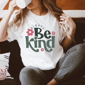 May include: White t-shirt with the text "Always Be Kind" in green lettering with pink flowers. The text is in a retro font style.