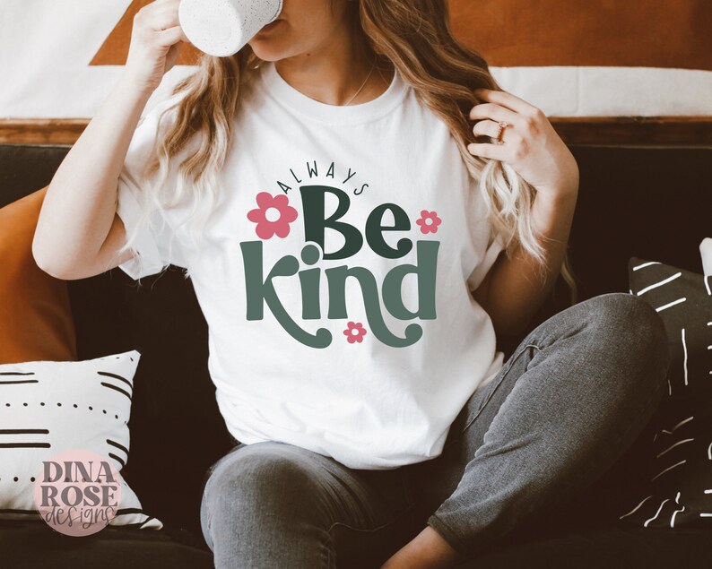 May include: White t-shirt with the text "Always Be Kind" in green lettering with pink flowers. The text is in a retro font style.