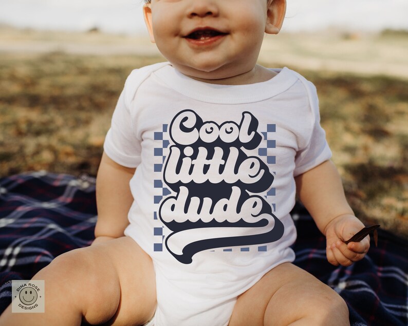 May include: A white baby onesie with a blue and white checkered background and the text "Cool little dude" in a retro font.