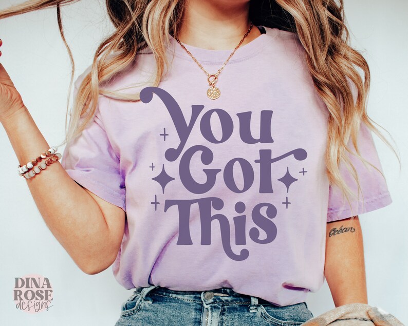 Puede incluir: Una camiseta morada con el texto "You Got This" en una fuente retro. El texto est&aacute; en color morado oscuro y est&aacute; rodeado de peque&ntilde;as estrellas blancas.