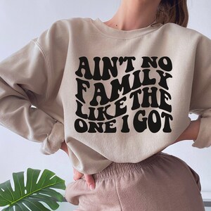 Pu&ograve; includere: Una felpa beige con il testo "Ain't no family like the one I got" in lettere nere in stile retr&ograve;.