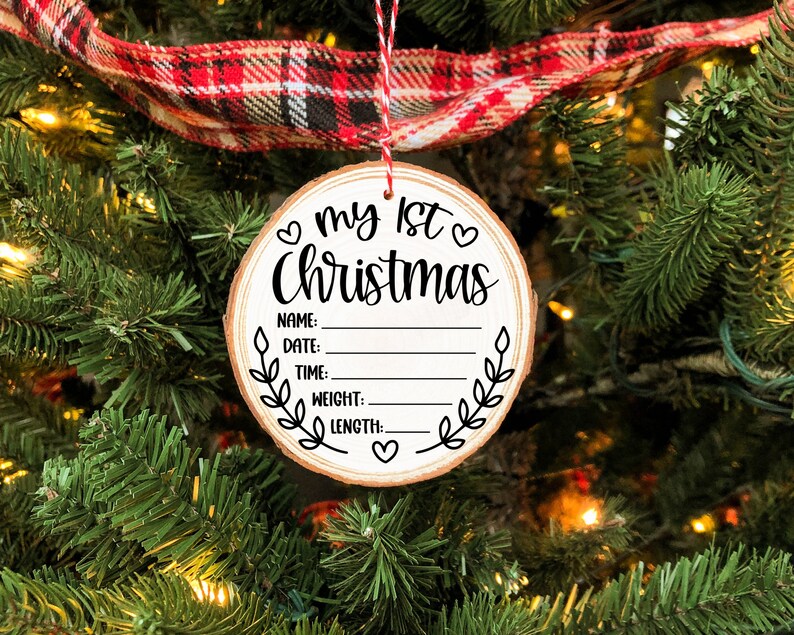 Pu&ograve; includere: Un ornamento rotondo in legno con il testo "♡ my 1st ♡ Christmas" e righe vuote per "Name", "Date", "Time", "Weight", e "Length".