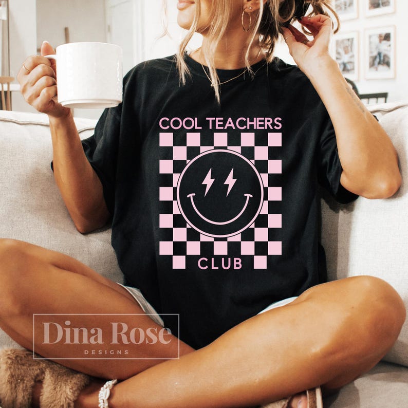 May include: A black t-shirt with a pink checkered pattern and a pink smiley face with lightning bolts. The text "COOL TEACHERS CLUB" is printed in pink on the shirt.