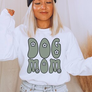 May include: White sweatshirt with a green retro-style graphic that says "DOG MOM" with white flowers.