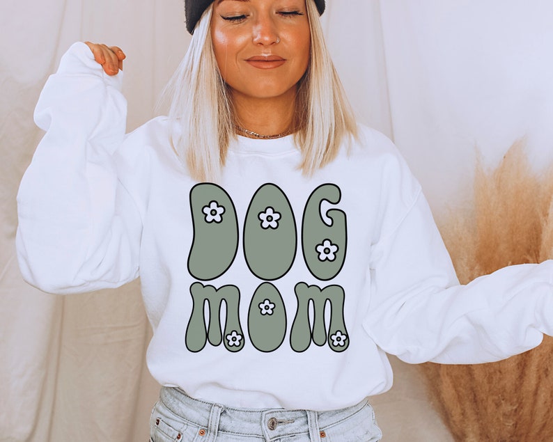 May include: White sweatshirt with a green retro-style graphic that says "DOG MOM" with white flowers.