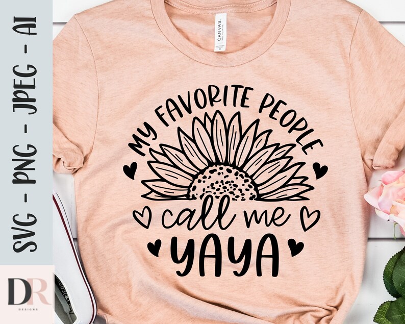 K&ouml;nnte beinhalten: Ein pfirsichfarbenes T-Shirt mit einer schwarzen Sonnenblumengrafik und dem Text "Meine Lieblingsmenschen nennen mich Yaya" mit Herzen.