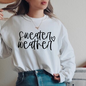 Puede incluir: Sudadera blanca con texto negro que dice "sweater weather" con un peque&ntilde;o s&iacute;mbolo de coraz&oacute;n.