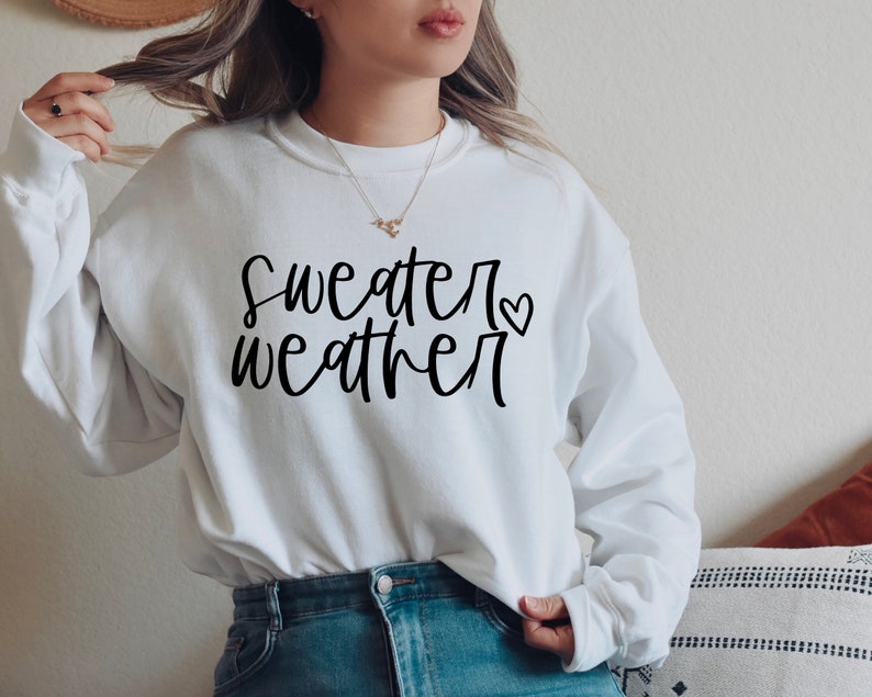 Puede incluir: Sudadera blanca con texto negro que dice "sweater weather" con un peque&ntilde;o s&iacute;mbolo de coraz&oacute;n.