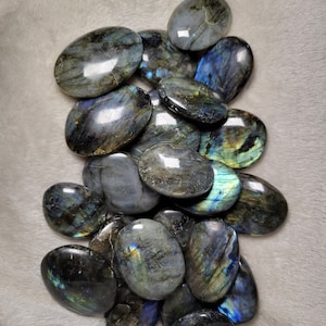 May include: A collection of oval-shaped labradorite stones, each with a unique iridescent sheen. The stones are a mix of dark gray, blue, and green colors, with flashes of gold and silver.