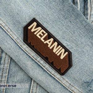 Peut inclure: Un &eacute;cusson brod&eacute; marron et noir avec le mot "MELANIN" en lettres blanches sur une veste en jean.