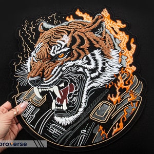 May include: Embroidered patch depicting a ferocious tiger with orange and white fur, roaring with bared fangs. The tiger is surrounded by flames and a detailed black and white background.