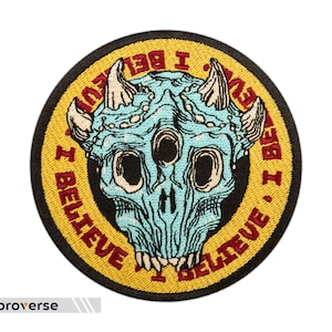 May include: A round, yellow and black embroidered patch with a blue and white skull with horns in the center. The text around the skull reads "I Believe I Believe".