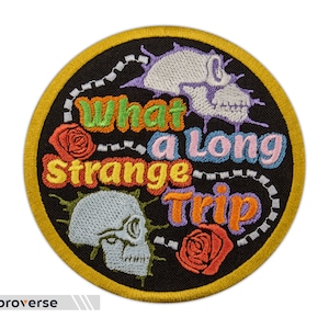 Puede incluir: Un parche redondo bordado de color negro con un borde amarillo. El parche presenta el texto "What a long strange trip" en letras de colores estilizadas. El parche también incluye dos diseños de calaveras y huesos cruzados y dos rosas.